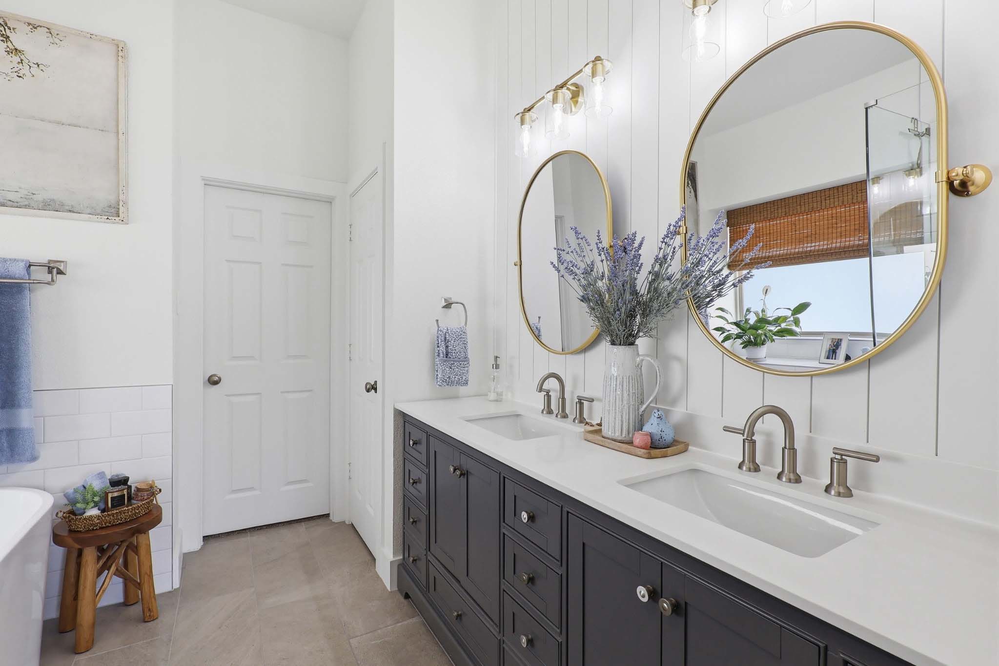 Remodeled bathroom with gray double vanity, white shiplap wall, and round gold mirrors