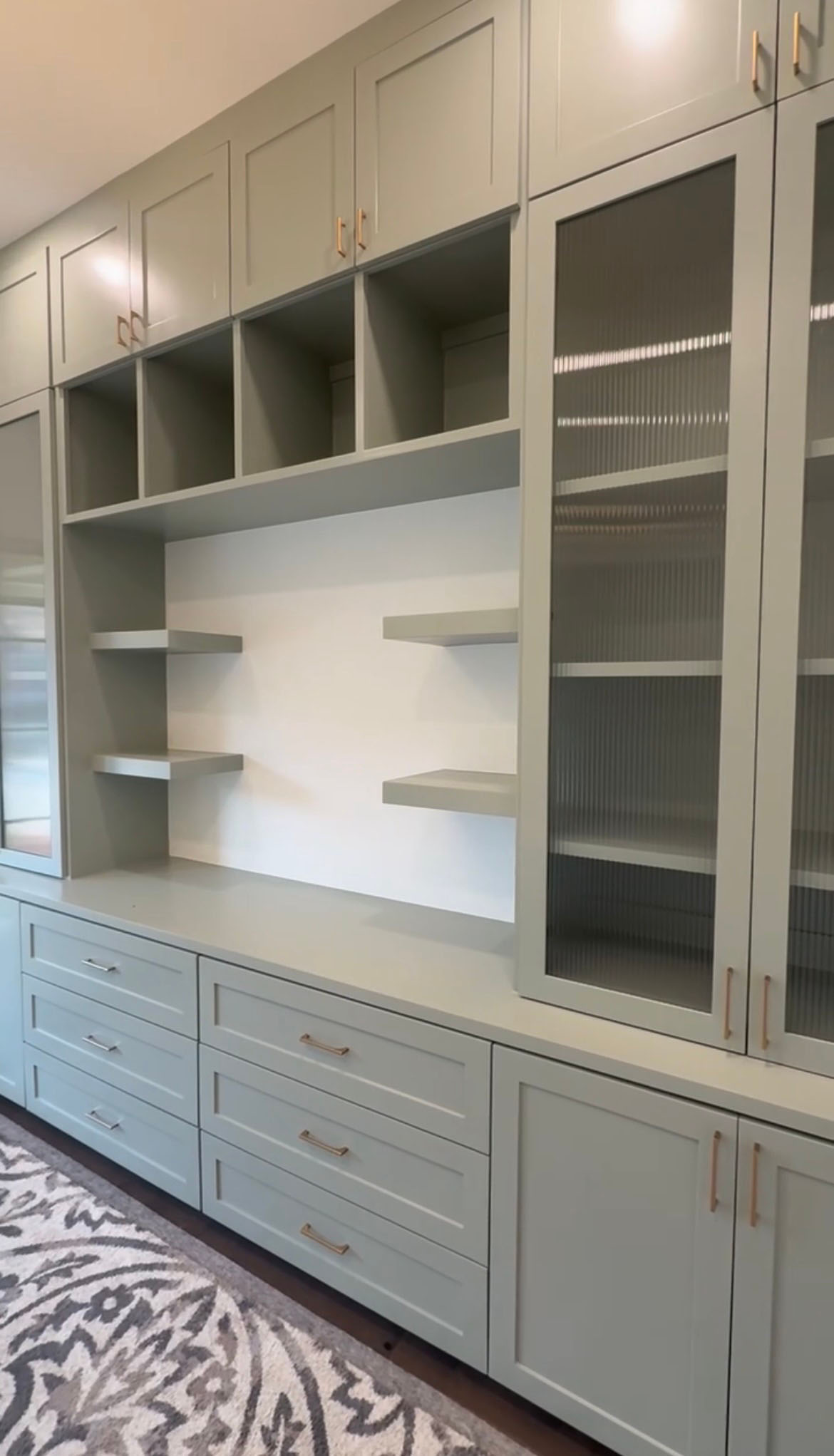 Custom sage green built-in cabinetry with fluted glass doors, open shelving, and gold hardware