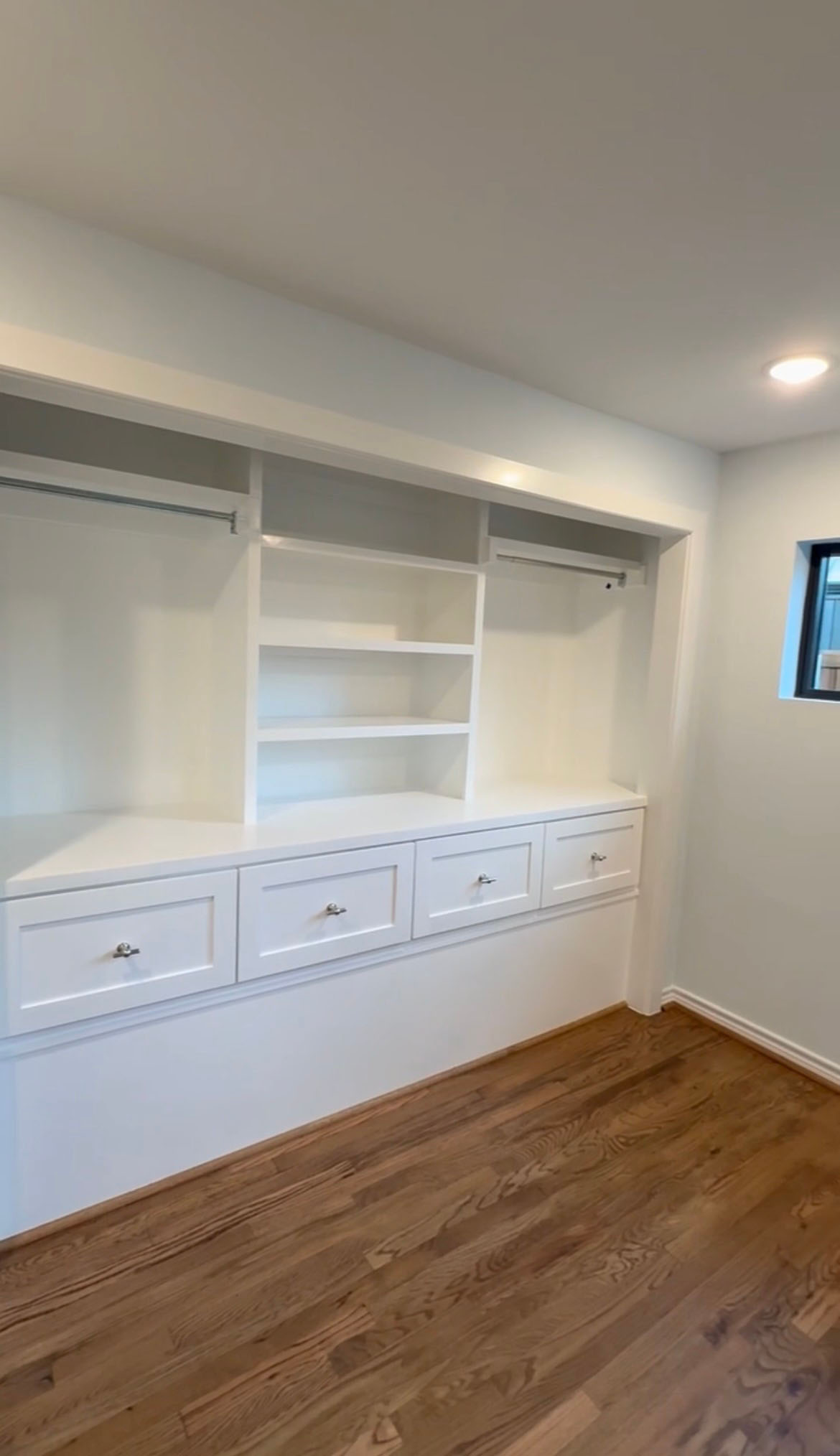 Custom white built-in closet with drawers, open shelving, and hanging rods