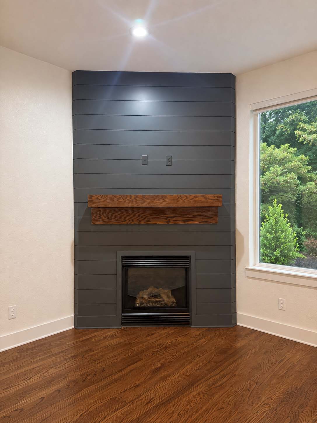 Corner fireplace with gray shiplap surround and stained wood mantel