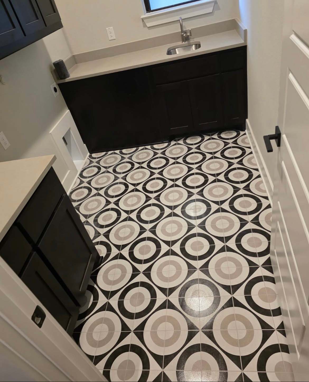 Remodeled laundry room with black cabinets, quartz counter, and black and white geometric tile floor