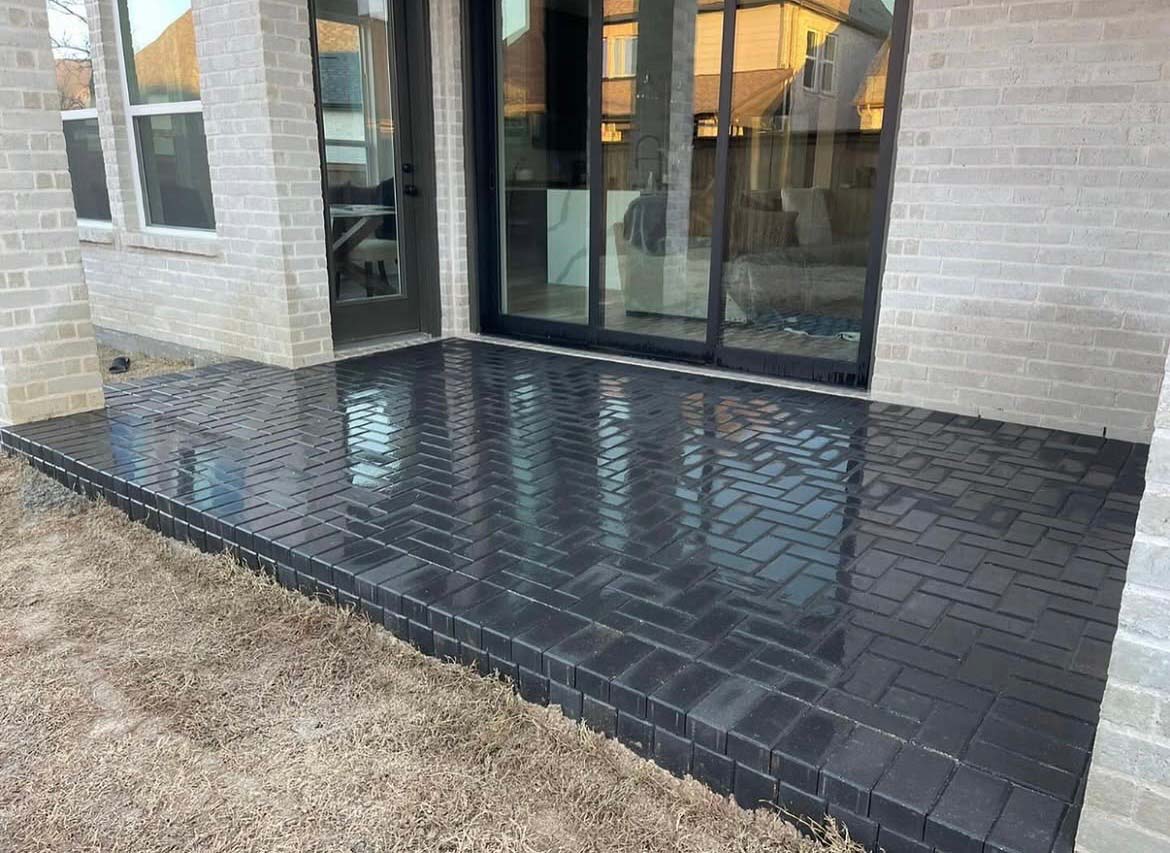 New herringbone black brick paver patio behind white brick home
